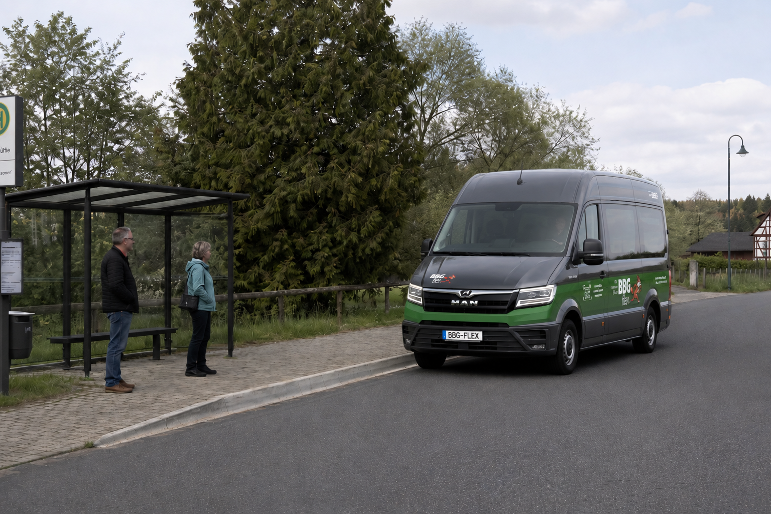 Ein heller BBG-flex Kleinbus hält an einer ländlichen Bushaltestelle, an der ein Fahrgast wartet.